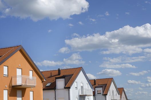 roofs of houses in different colors under blue sky with clouds above