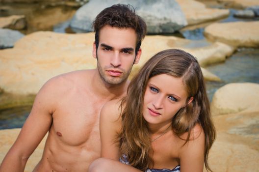 Young romantic couple of boyfriend and girlfriend in swimsuit on rocks by the water