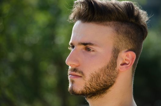 Portrait of handsome young man outdoors in nature, looking to a side