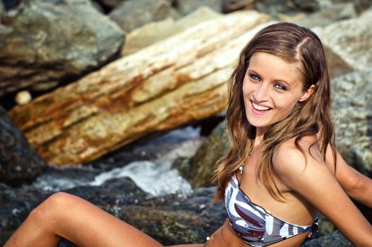 Pretty brunette girl, blue eyes, sitting on rocks in a river smiling