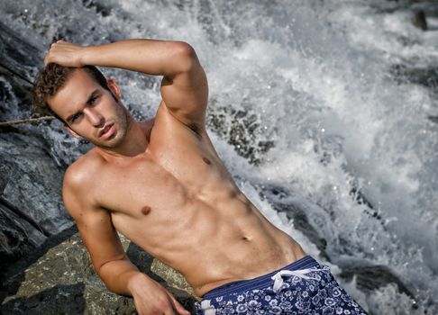 Attractive young man naked wearing a swimsuit near waterfall or river water