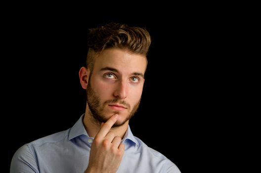 Attractive young man looking up, thinking, isolated on black background