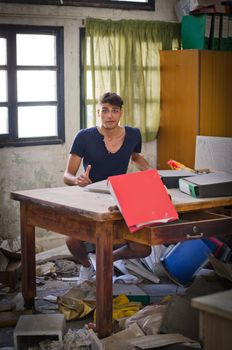 Young man in very messy office looking lost or confused