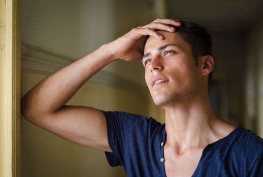 Handsome young man in hallway looking up, thinking and holding his head