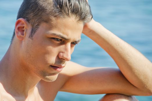 Handsome young man thinking next to the sea with wet hair, hand on his head
