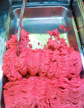 Raw minced meat in a metal tray with a metal scoop