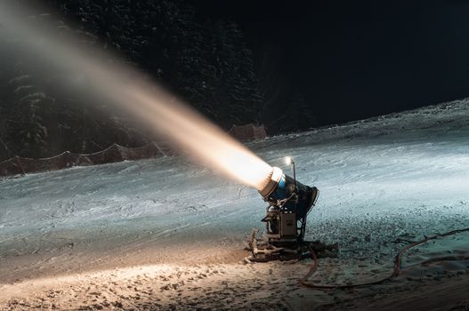Working snow cannon at night on ski slope.