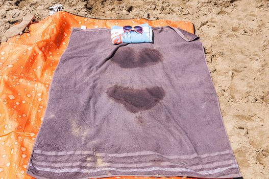 A towel with wet spots laying on the beach.