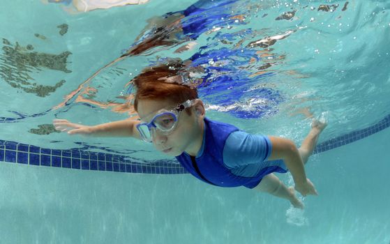  child holding breath and swimming underwater in pool
