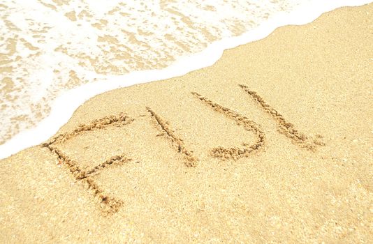 A warm tropical beach wand waves and Fiji written in the sand 