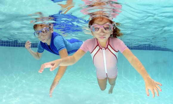 two children swimming underwater in pool in pink and blue