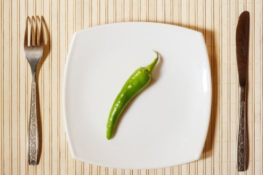 Fresh green pepper on a white square plate.