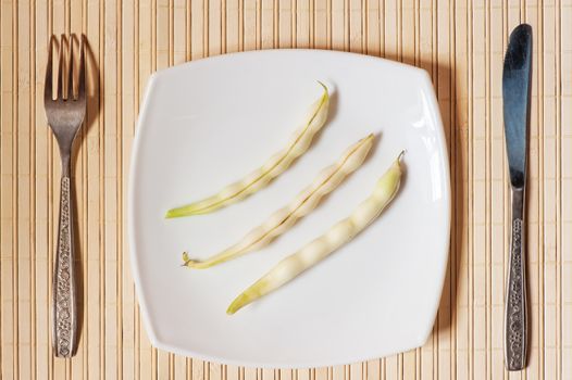 Three pods of beans on a white square plate.