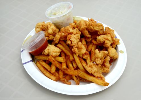 conch fritters on a paper plate with french fries on a white table