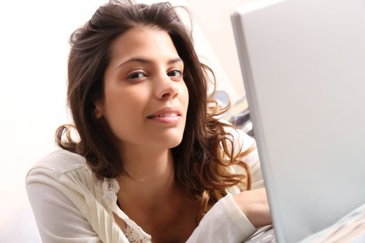 A young girl laying on the bed and surfing on the Internet with a Laptop.