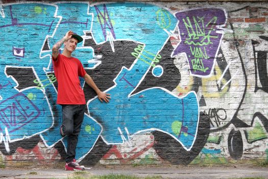 A greeting young Rapper greeting in front of a Graffiti wall.