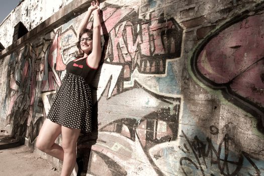 A vintage style dressed girl leaning at a graffiti wall and enjoying the sunlight.