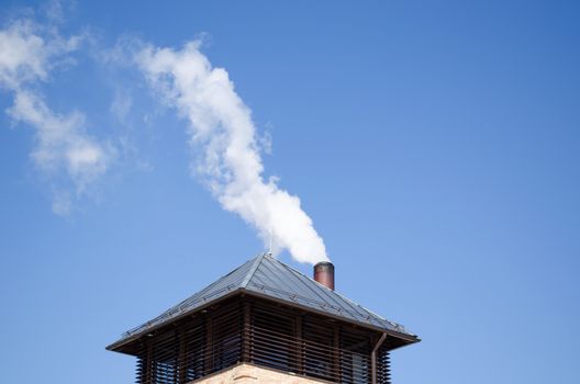 modern tin covered roof and white smoke rise from round chimney pipe on background of dark blue sky.