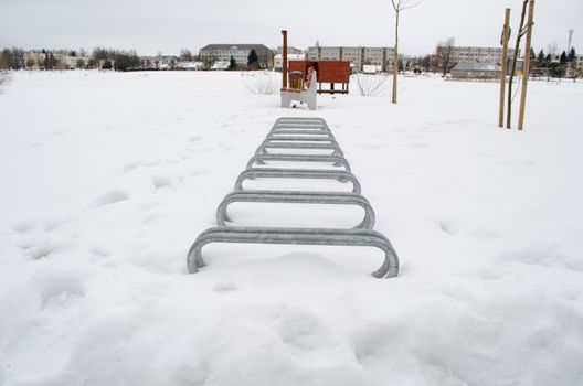 steel bicicle parking place covered with snow near park lake beach in winter.