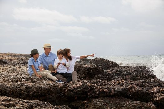 happy family sitting on rock and watching the ocean waves holiday 