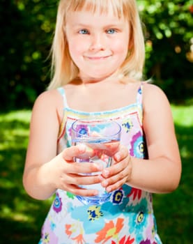 Little girl holding glass of water outdoors, focus on glass