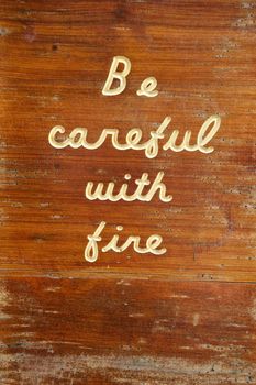 An old, weathered and worn, outdoor, wooden sign with "Be Careful With Fire" carved into it that shows signs of aging.