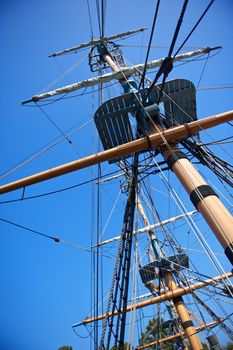 The rigging and masts of an old sailing ship against a blue sky