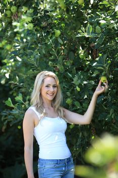 Standing blond woman holding a fruit in the garden
