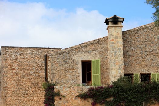 Exterior facade of a stone building with a chimney and windows with green shutters