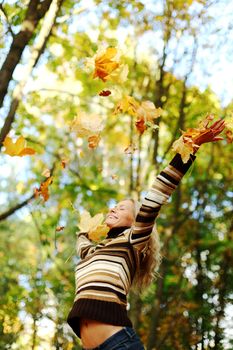 woman drop up leaves in autumn park