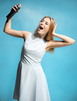 Beautiful girl in a white dress holding a bottle with hairspray