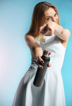 Beautiful girl in a white dress holding a bottle with hairspray