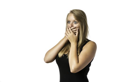 Shocked young girl in black shirt who is afraid and keeps up with eyes wide open hand over her mouth, isolated on white background