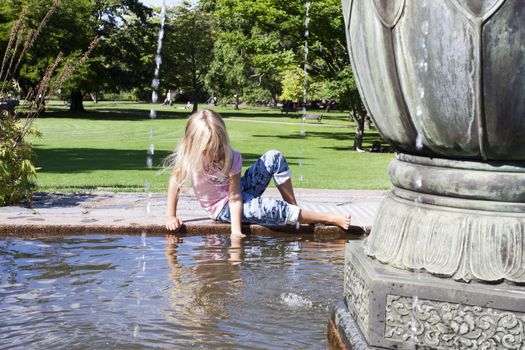 A young girl sitting on the edge of a fountain playing with the water