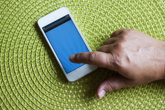 A smart phone on a green background and a hand pointing at it