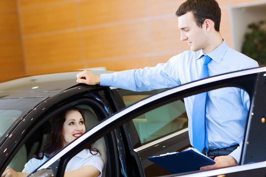 Attractive woman at car salon with consultant choosing a car