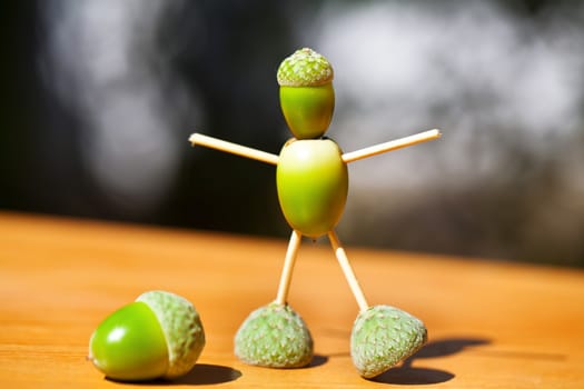 Little man made of green acorns on wood