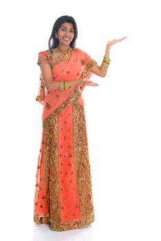 Full body cheerful traditional Asian Indian woman in sari arm out showing empty space, isolated on white background.