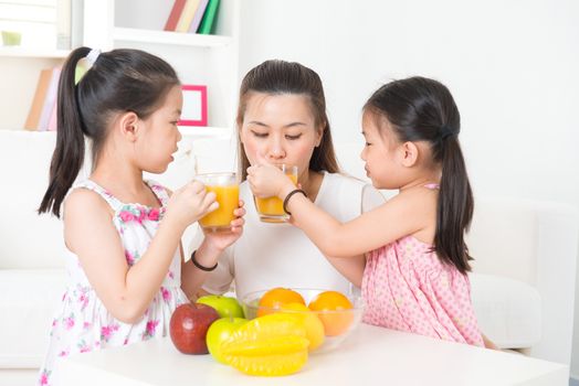 Asian family drinking orange juice. Happy Asian parent and children enjoying cup of fresh squeeze fruit juice at home.