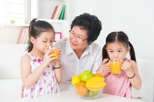 Asian family drinking orange juice. Happy Asian grandparent and grandchildren enjoying cup of fresh squeeze fruit juice at home.