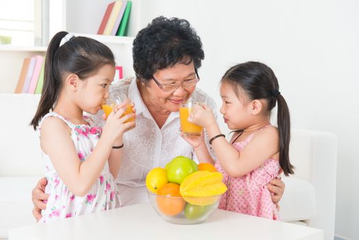 Asian family drinking orange juice. Happy Asian grandparent and grandchildren enjoying cup of fresh squeeze fruit juice at home. Healthcare concept.