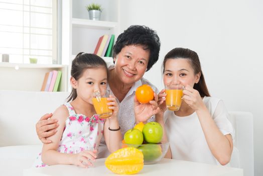 Asian family drinking orange juice. Happy Asian grandparent, parent and grandchild enjoying cup of fresh squeeze fruit juice at home.