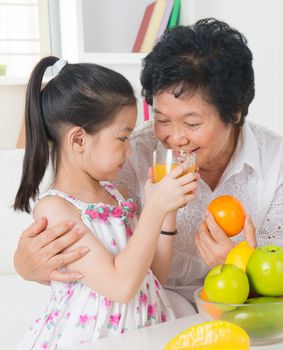 Asian family drinking orange juice. Happy Asian grandchild sharing cup of fresh squeeze fruit juice with grandmother at home.