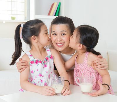 Happy Asian mother and daughters drinking milk at home, children kissing mother. Parent and children. Beautiful family model.