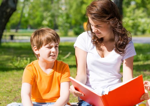 boy and a woman in a summer park reading a book together