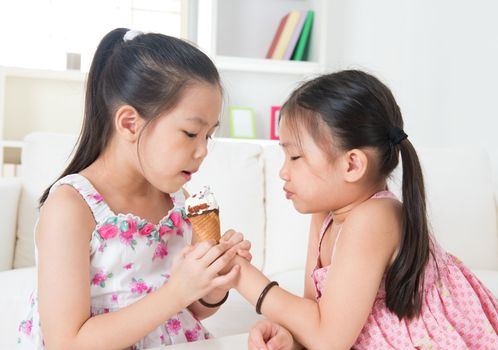 Eating ice cream cone. Asian girls sharing an ice cream. Beautiful children model at home.