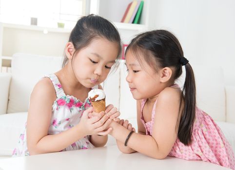 Eating ice cream cone. Asian children sharing an ice cream. Beautiful girls model at home.