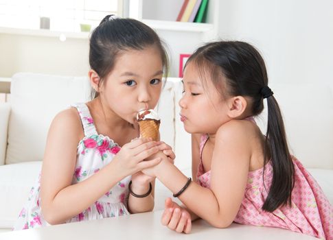 Eating ice cream cone. Asian children sharing an ice cream at home.  Beautiful girls model.