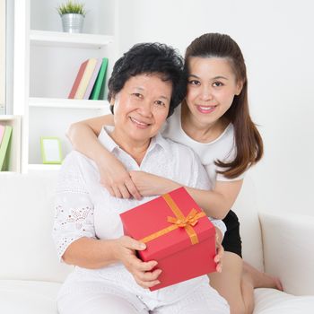 Senior woman receiving a gift from adult daughter, beautiful Asian family at home.