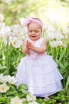Little girl in an elegant dress to stand near blossoming tulips